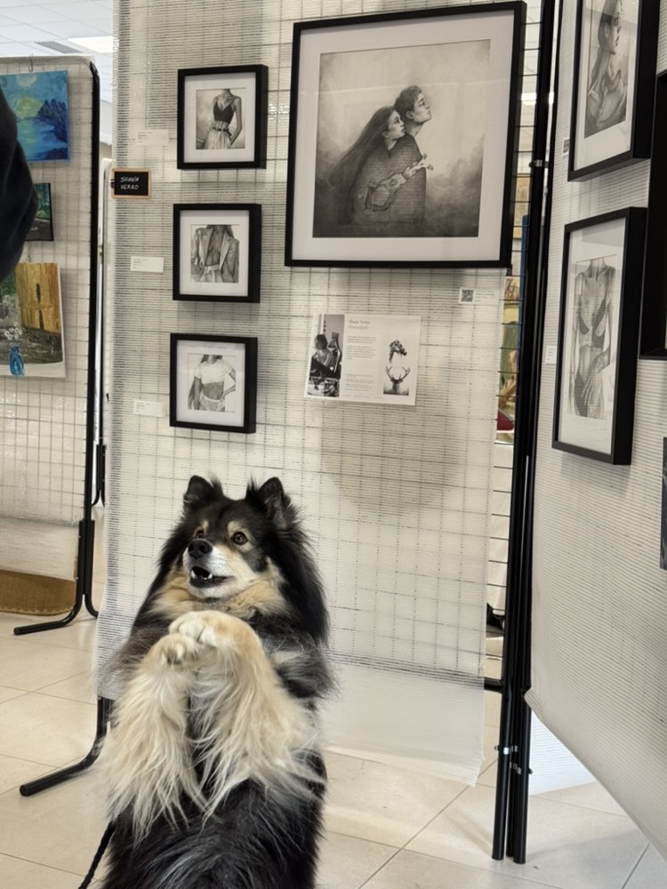 Stand d'exposition avec des portraits au graphite encadrés, et Sunlight assis devant